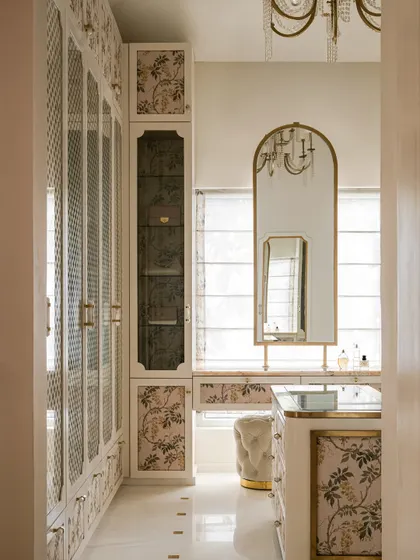 A different angle of the walk-in closet, showing the arched vanity mirror with brass trim and a plush tufted ottoman, creating a refined and glamorous dressing area.