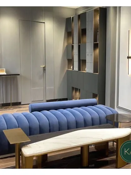 A vibrant blue channel-tufted sofa designed as the centerpiece for a modern apartment. The attached marble and wood bench offers a unique, integrated surface, blending functionality with a bold design statement.