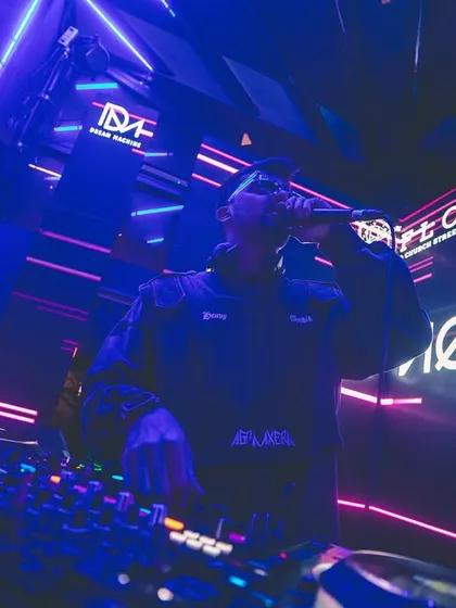 Hyping the crowd on the mic from the DJ booth, surrounded by neon lights. My style is interactive, ensuring everyone feels like a part of the show.