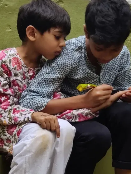 An older child gently applies mehendi to a younger child's hand. These moments of shared tradition and quiet connection are what make our festival celebrations so special.