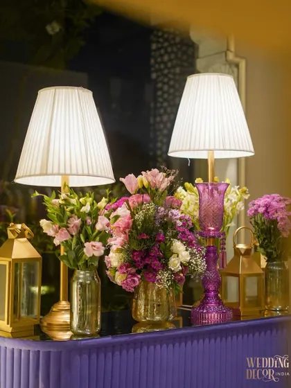 Elegant details from the entrance corridor. The side tables feature pleated lampshades, golden lanterns, and beautiful bouquets of pink and purple flowers.