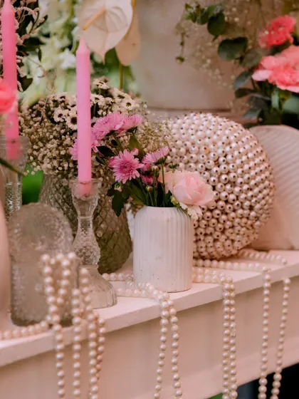 Pink candles and pearl-textured spheres are mixed with fresh flowers to create a detailed and aesthetically pleasing decor vignette.