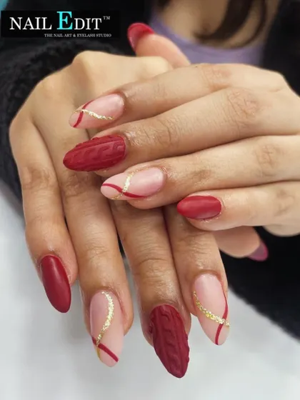 A cozy and unique design featuring a matte red "sweater" texture on accent nails. This is paired with a sheer nude base, red lines, and a touch of gold glitter for a stylish, autumnal look.