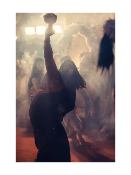 A woman lost in the moment during the Dhunuchi dance. The smoke and warm light create a divine, otherworldly atmosphere that is central to the Sandhya Aarti.