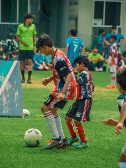 Two young players challenge for the ball near the Sar Sportz banner.