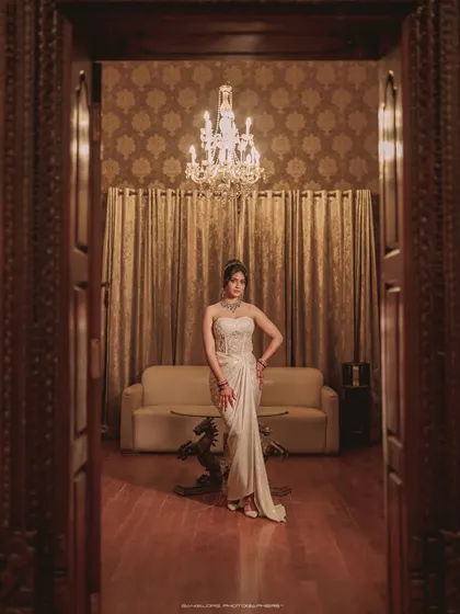 A dramatic, full-length portrait of the bride in a stunning white gown. The framing through the doorway and the grand chandelier add a touch of regal elegance.