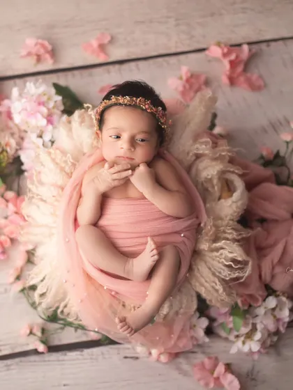 This little doll is wide awake and surrounded by soft pink blossoms. The floral elements perfectly complement her delicate features and pink swaddle.