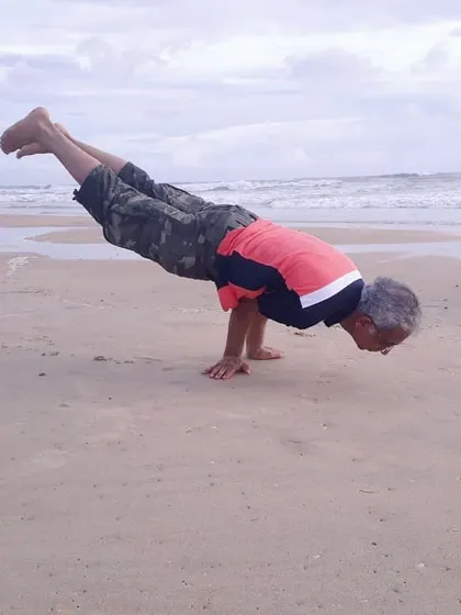 Performing Mayurasana (Peacock Pose) on the beach. This advanced arm-balancing pose shows that with consistent practice, you can maintain strength and vitality at any age.
