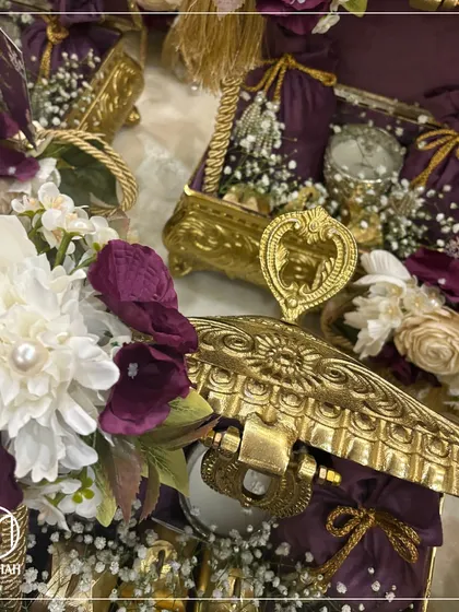 A detailed shot of the Rajwada Chest, focusing on the intricate metalwork, the heart-shaped clasp, and the rich floral arrangements. Every element is chosen to exude luxury.