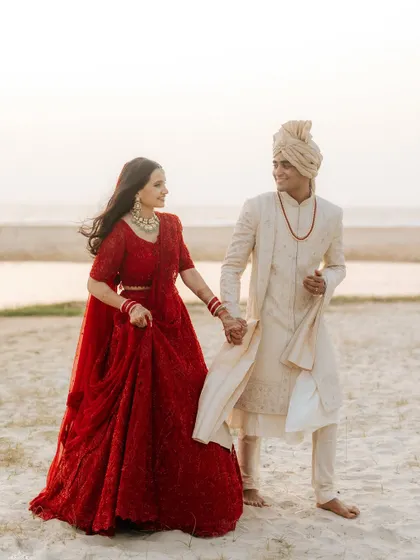 A classic portrait of the couple walking hand-in-hand on the beach, showcasing their elegant wedding attire.