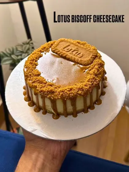 Our signature Lotus Biscoff Cheesecake, held up to show the beautiful caramel drip and generous layer of Biscoff crumbs. This is pure, unadulterated dessert heaven.