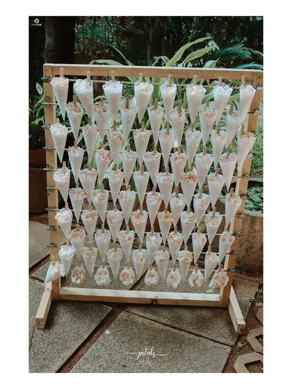 A creative and interactive detail for a wedding entrance. A wooden stand holds cones filled with fresh flower petals for guests to shower the couple with blessings as they arrive.
