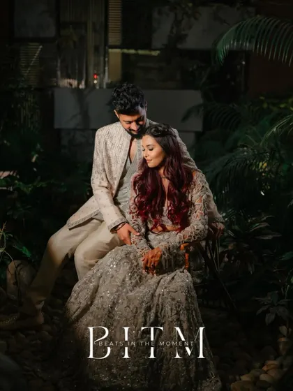 A stylish portrait of the couple seated in a lush, green setting at night. The dramatic lighting and their elegant poses create a sophisticated and romantic image.