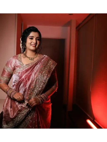 An elegant portrait of the bride in a beautiful pink saree, captured in a warmly lit corridor. Her happy and confident smile shines through.