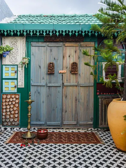 The eclectic and colorful entrance to a home, featuring distressed wooden doors, a tiled roof, and geometric flooring.