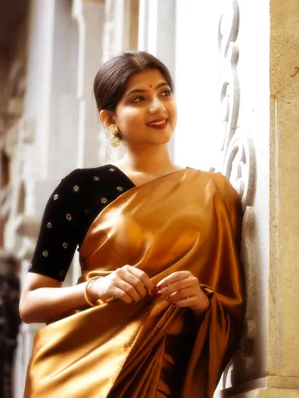 A smiling portrait in a shimmering gold satin saree. The focus is on creating a radiant and approachable look, letting the saree's luxurious texture speak for itself.