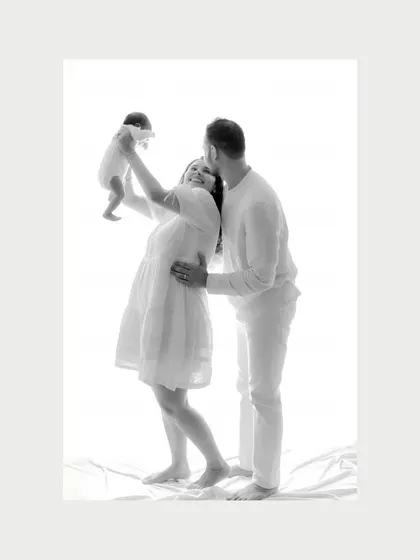 A moment of pure joy as the mother lifts her newborn into the air while the father looks on lovingly. This black and white image captures the dynamic happiness of a new family.