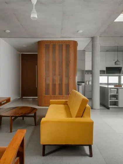 The living area of the LUCID residence showcases our minimalist approach using a humble material palette. Exposed concrete ceilings and vitrified tile floors create a neutral backdrop, punctuated by a custom wooden screen that separates the foyer.
