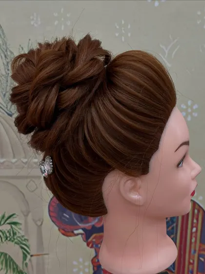 A high bun with braided details, beautifully executed by a student on a mannequin head. Practice is key to perfection.