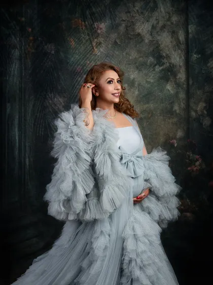 A beautiful close-up in a stunning grey ruffled gown. The painterly background and soft lighting create a sophisticated and elegant mood for this maternity portrait.