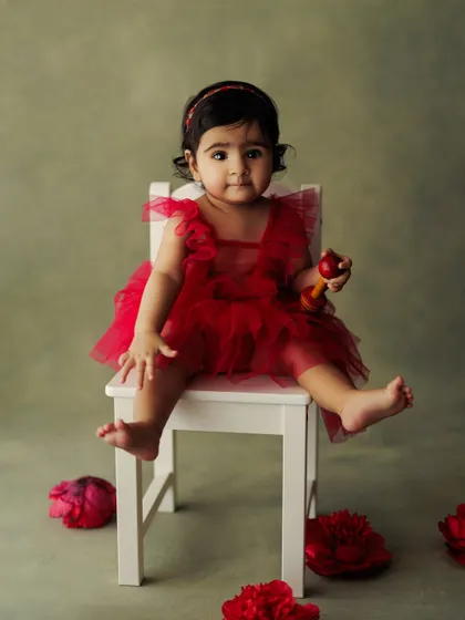 A sweet and classic portrait of a baby girl in a red dress, holding a small toy. A perfect image to celebrate a special milestone.
