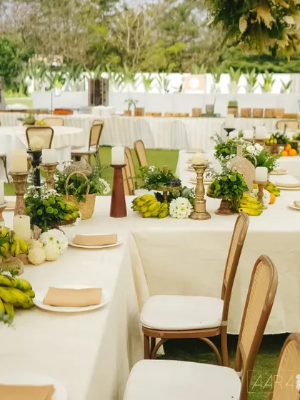 The tables at our 'Easy Breezy Brunch' are adorned with centerpieces of fresh bananas, grapes, and apples, mixed with simple white flowers. The decor embraces a monochromatic palette of ivory, beige, and green for a calm, natural feel.