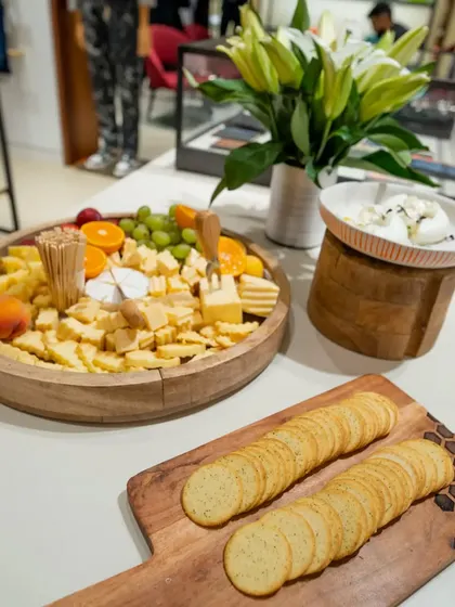A clean and minimalist cheese board setup for a Paul Smith store event. The wooden platter features a selection of cheeses, crackers, and fresh fruits, reflecting the brand's sophisticated style.