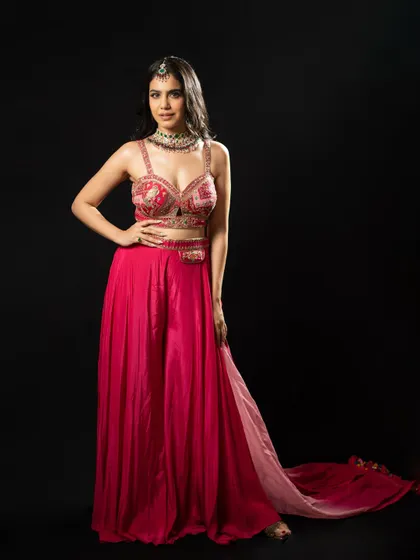 A full-length studio portrait in the pink and red sharara, showcasing a powerful and confident pose.