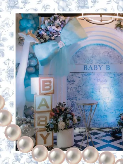 A close-up of the Dior-inspired photo booth, featuring a large blue bow, 'BABY' blocks, and a giraffe prop, all framed with a pearl border effect for extra elegance.