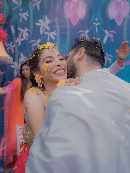 A joyful, candid embrace during a colorful Haldi ceremony, capturing the raw emotion and fun of the moment.