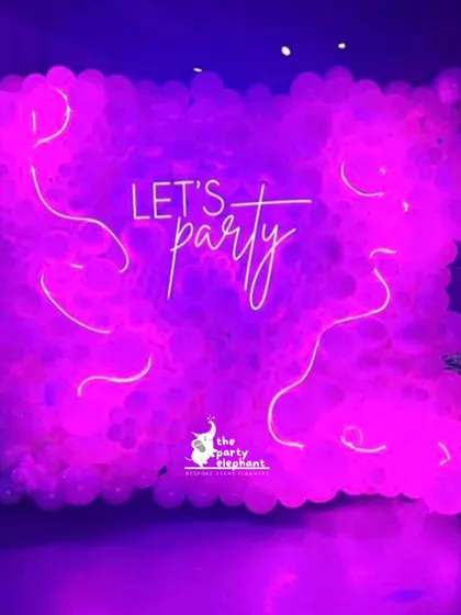 A 'Let's Party' neon sign against a wall of purple balloons created a simple yet highly effective photo backdrop, perfect for capturing the fun and energetic vibe of the night.