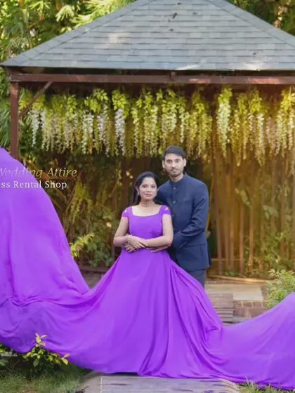 A couple poses in a garden setting with a vibrant purple flying gown. The fabric is arranged to create a wide, dramatic spread, filling the frame with color.