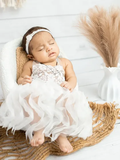 A little angel sleeping in a beautiful white lace dress. The boho-chic setup with pampas grass and macrame adds a soft, dreamy texture.