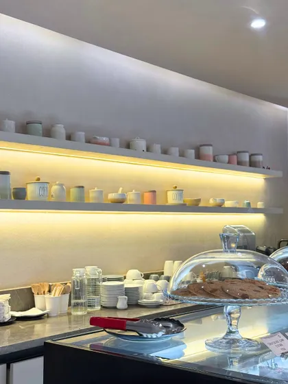A look at our counter, with cookies under a glass cloche and our collection of ceramic cups neatly arranged on backlit shelves.