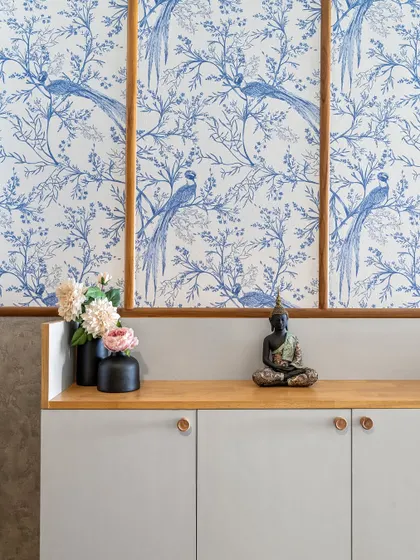 A close-up of the foyer console, topped with a serene Buddha statue and fresh flowers. The blue bird wallpaper adds a touch of classic elegance.