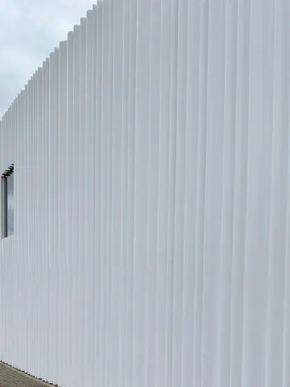 The corrugated white facade of a building at the Vitra Campus by SANAA. The simplicity of the form is animated by the rhythmic play of light and shadow across its surface.