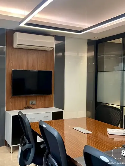 Another view of a conference room, showcasing a TV mount on a paneled wall with integrated cabinetry. The linear overhead lighting provides even, glare-free illumination for presentations and video calls.