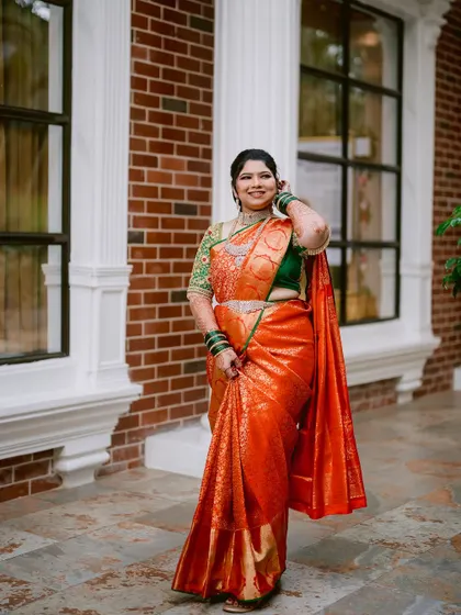A full-length portrait of the bride, Prerna, showcasing her beautiful orange and green wedding saree.
