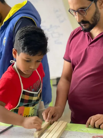 An instructor provides guidance as a young boy learns to sand a piece of wood, an important step for any woodworking project.