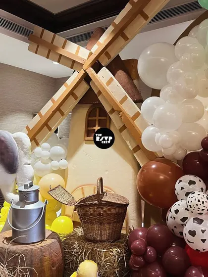 A detailed shot of the farm decor, showing a windmill prop, a basket, a milk can, and cow-print balloons.