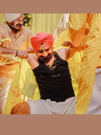 A candid shot of the groom during his Haldi, being playfully held by his friends. The vibrant colors of the turbans and outfits add to the festive atmosphere.
