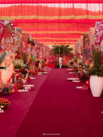 The long, dramatic aisle leading to the wedding area, flanked by large, hand-painted panels depicting traditional Indian art, creating an immersive cultural experience for guests.