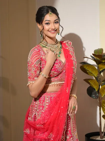 A full-length view of this stunning red lehenga look. It’s a perfect example of a classic bridal style with a contemporary, fresh-faced makeup application.
