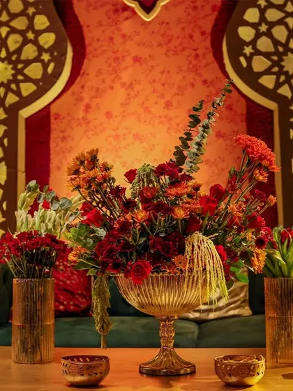 A close-up of a floral arrangement in front of a grand, illuminated arch. The details of the carved arch and the lushness of the flowers create a beautiful juxtaposition of hard architecture and soft nature.