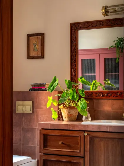 A detail shot of a bathroom in Calcutta, where a carved wooden mirror hangs above a vanity with terracotta tiles. A small, framed piece of art adds a personal touch, because I believe art belongs in every corner of a home.