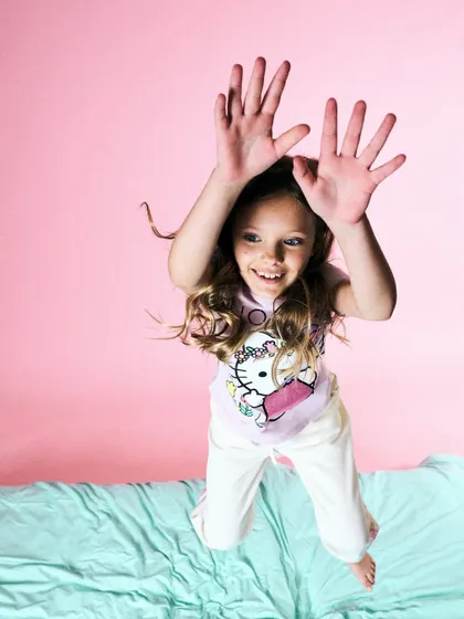 Pure, explosive energy. This shot of a girl jumping on a bed against a pink background is all about capturing a moment of absolute fun.