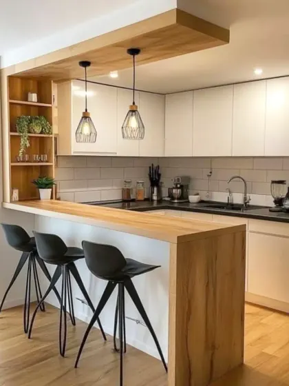 A minimalist kitchen design with a wooden breakfast bar, black stools, and simple white cabinets. The subway tile backsplash and industrial-style pendant lights complete the modern look.
