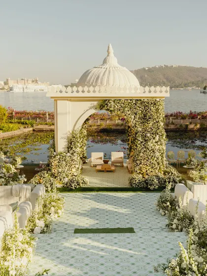 A serene mandap that appears to float on the waters of Udaipur. Framed by an arch of white florals, this design blends timeless tradition with the natural beauty of the location, creating a tranquil and elegant space for vows.