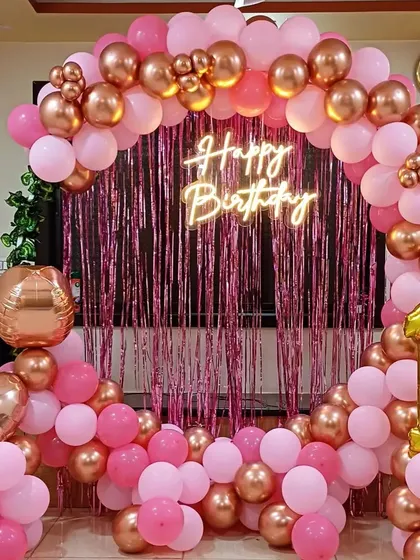 A pretty pink and rose gold theme for a first birthday. This home decoration includes a balloon arch, a shimmer backdrop, and a neon sign.