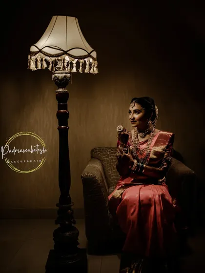 An artistic shot capturing the elegance of a bride before her ceremony. The warm lighting highlights the golden tones in her makeup and the rich texture of her silk saree.